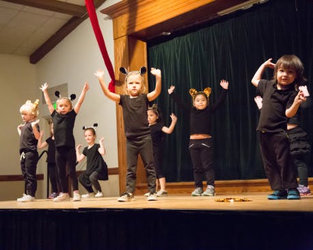 Children in black outfits and headbands performing on a stage