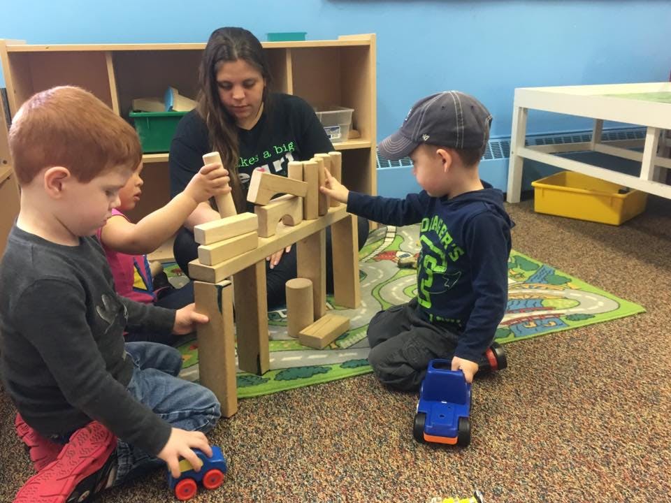 Adult and children playing with wooden blocks on a rug