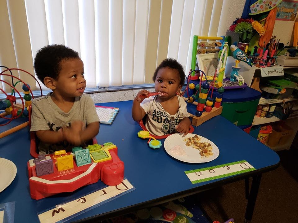 Two children sitting at a blue table, one eating and eating and one eating