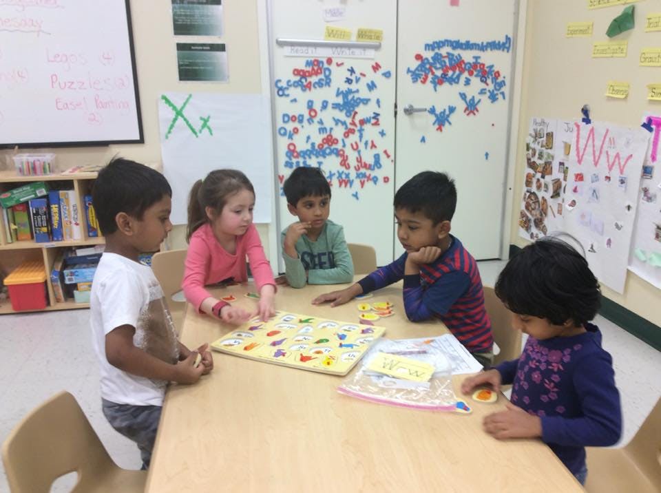 Five children playing with a puzzle at a table in a classroom