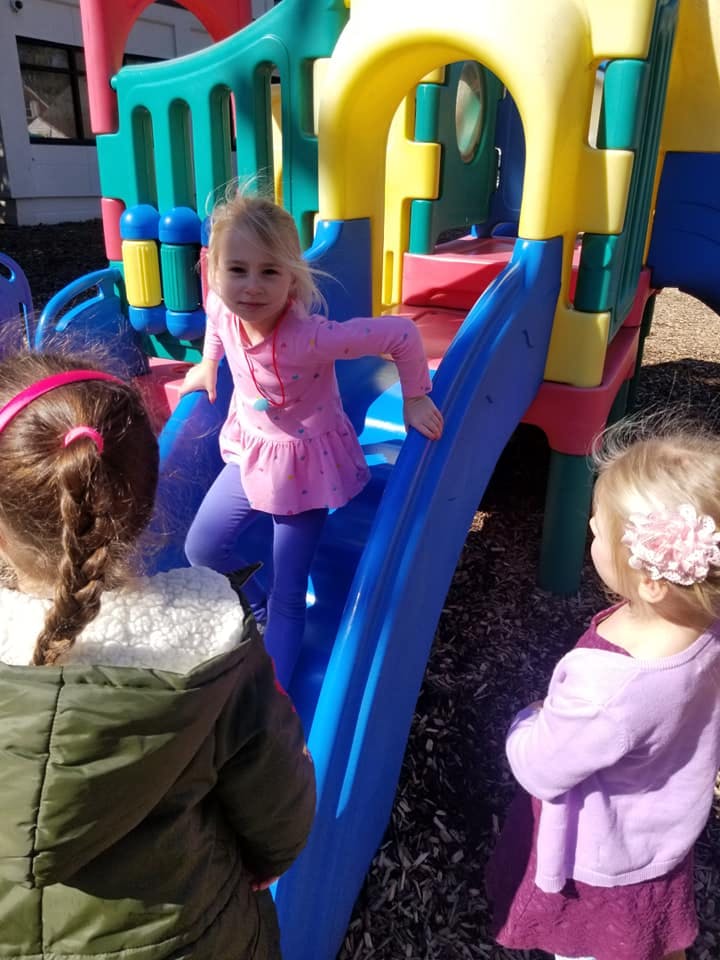 Child on a playground slide with two other children nearby