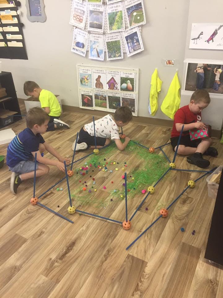 Three children playing on the floor with building toys and craft materials