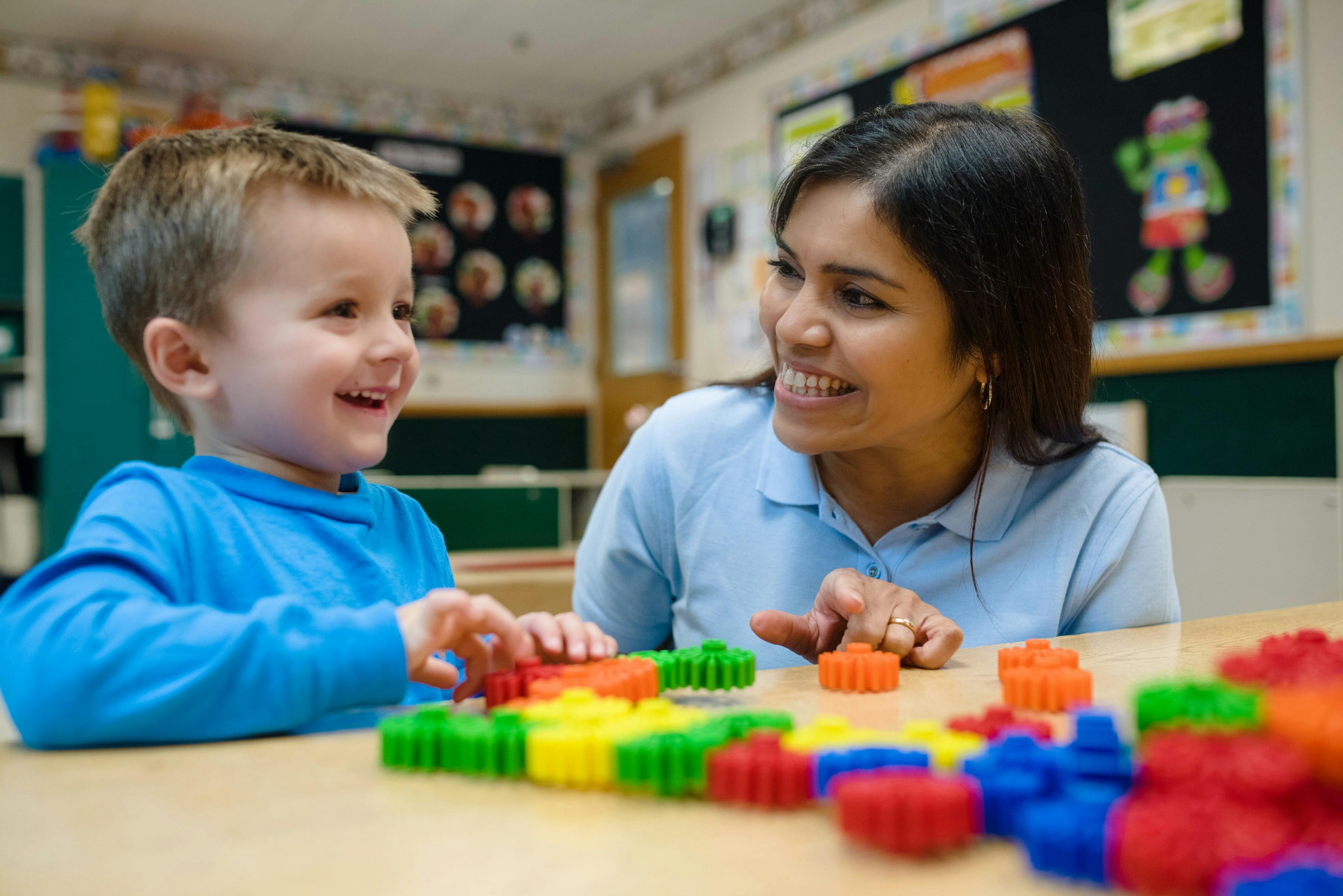 Adult and child playing with colorful interlocking toys in a classroom