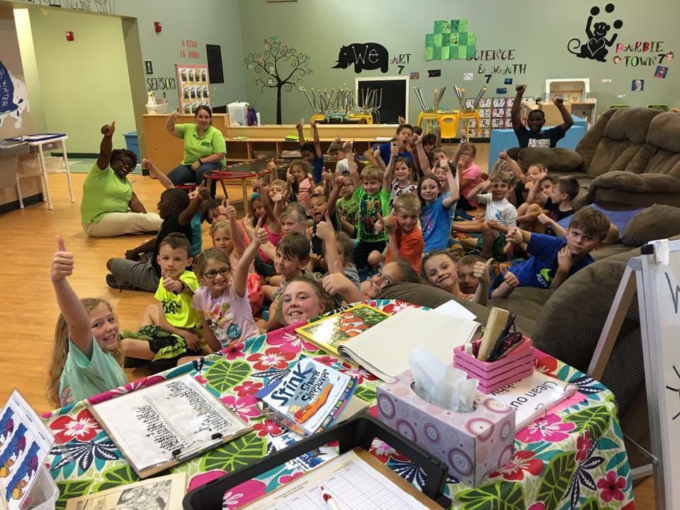 Group of children and adults in a classroom, many giving thumbs up