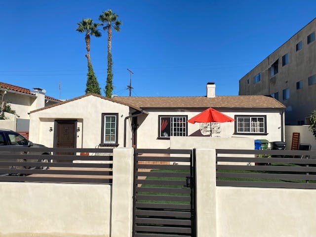 White house with a brown roof and a red umbrella in the yard