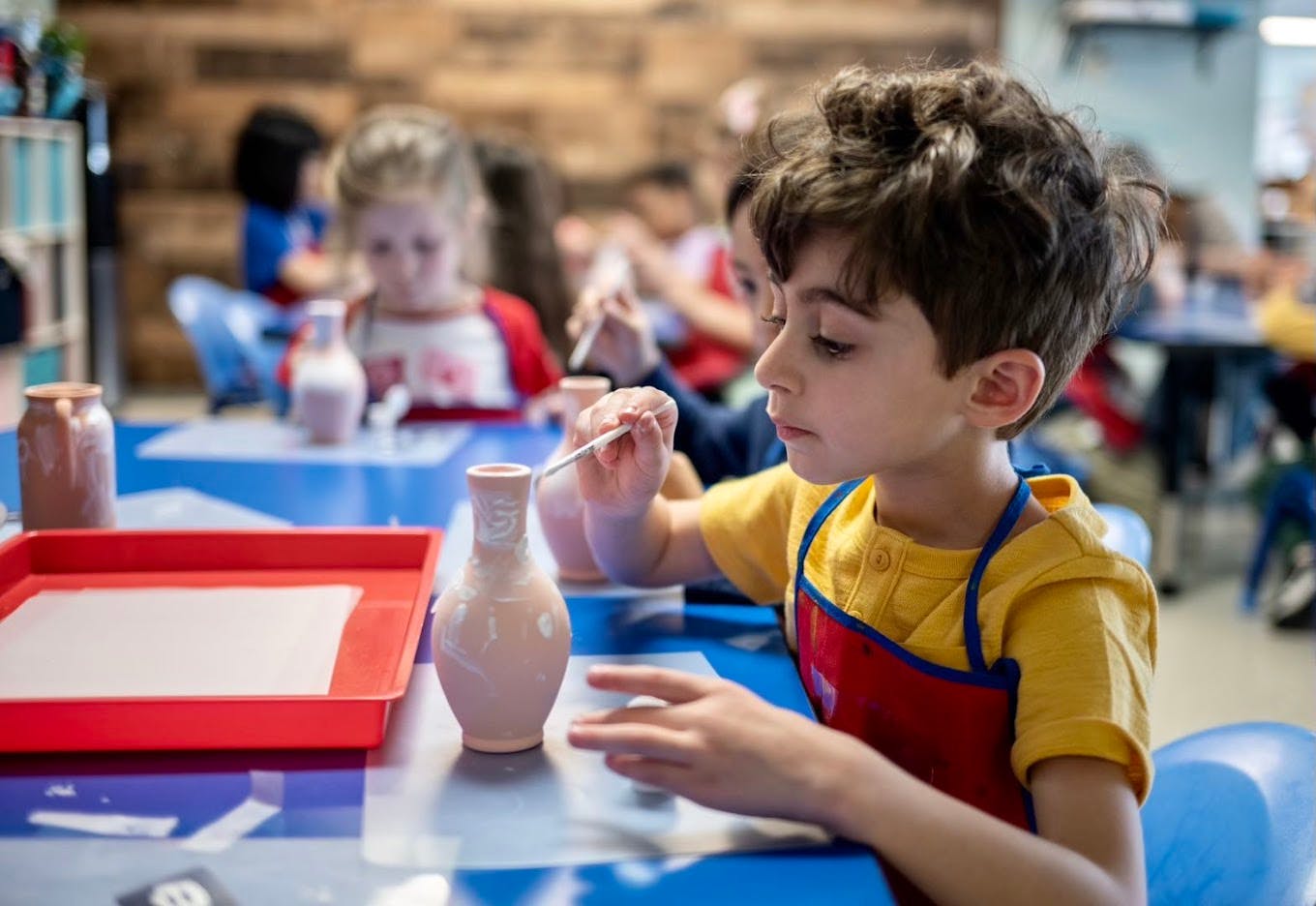 Child painting a ceramic vase in a classroom