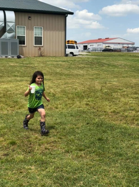 Child running in grass while holding a cup