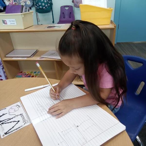 Child writing in a notebook with a pencil at a desk