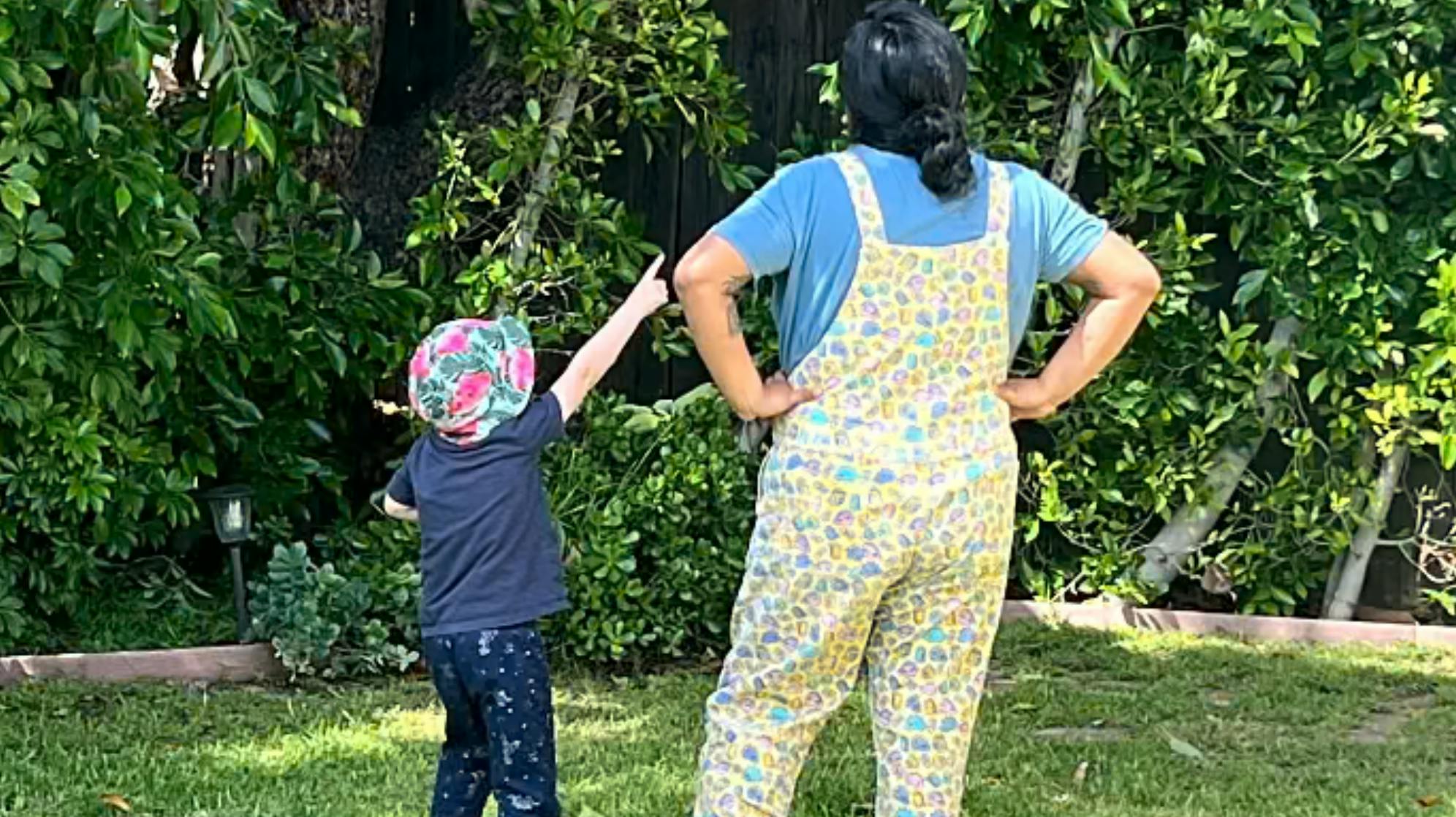 Person in overalls and child pointing up at trees