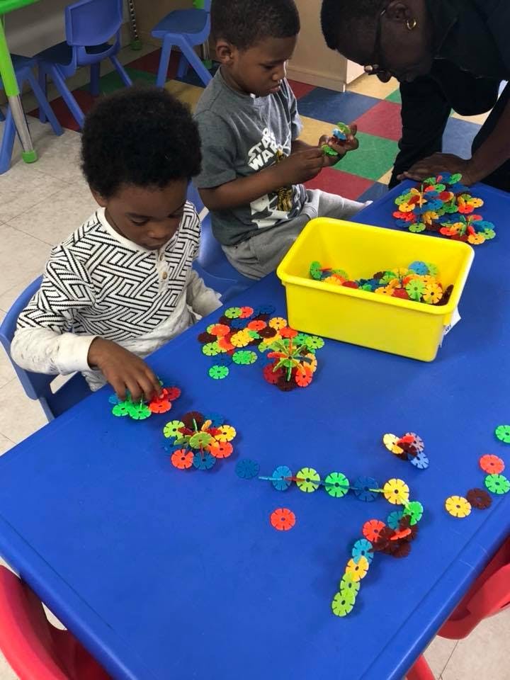 Two children and an adult playing with colorful interlocking toys at a blue table