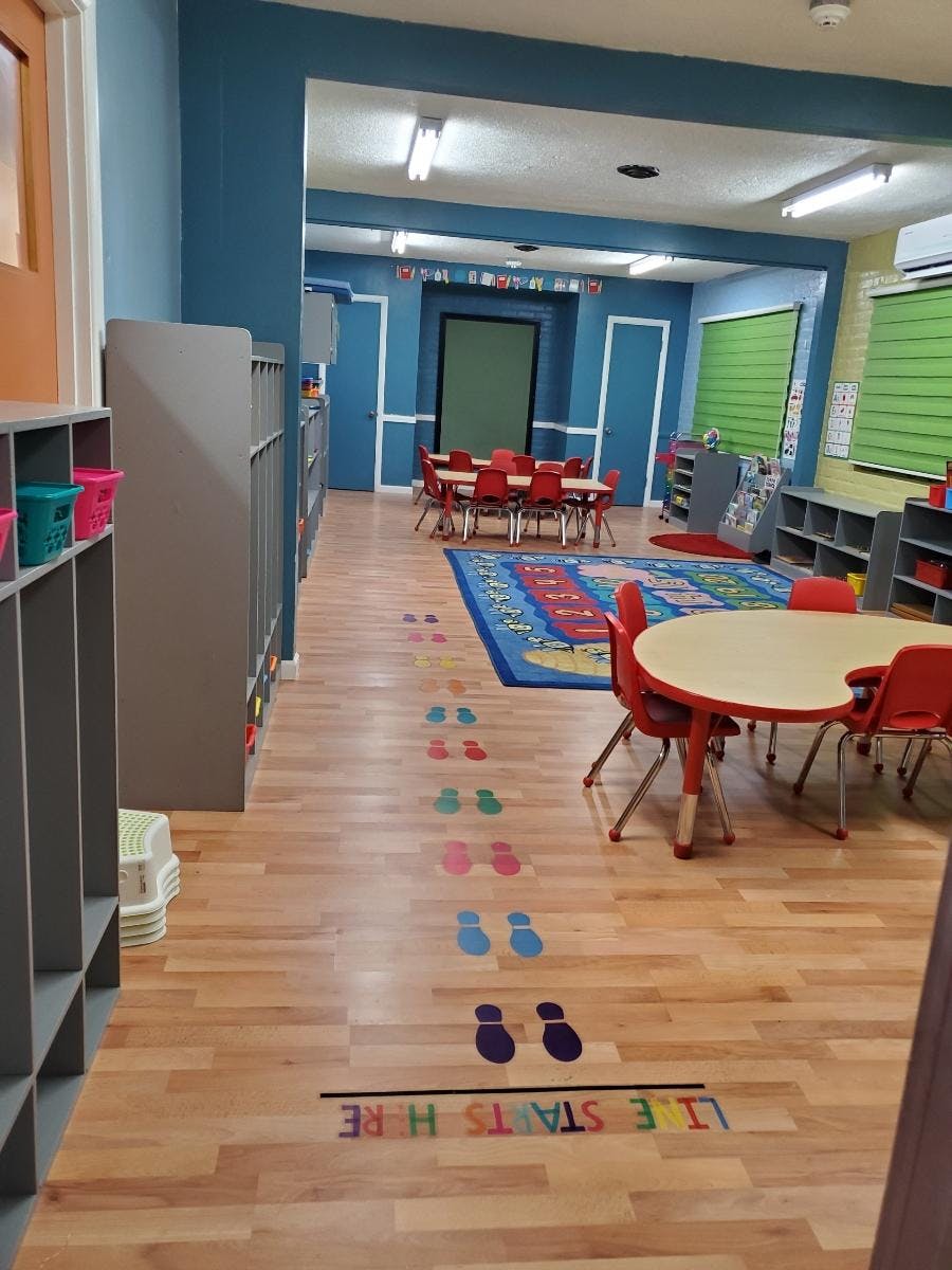 Classroom with small tables and chairs, colorful rug, and footprint decals on the floor