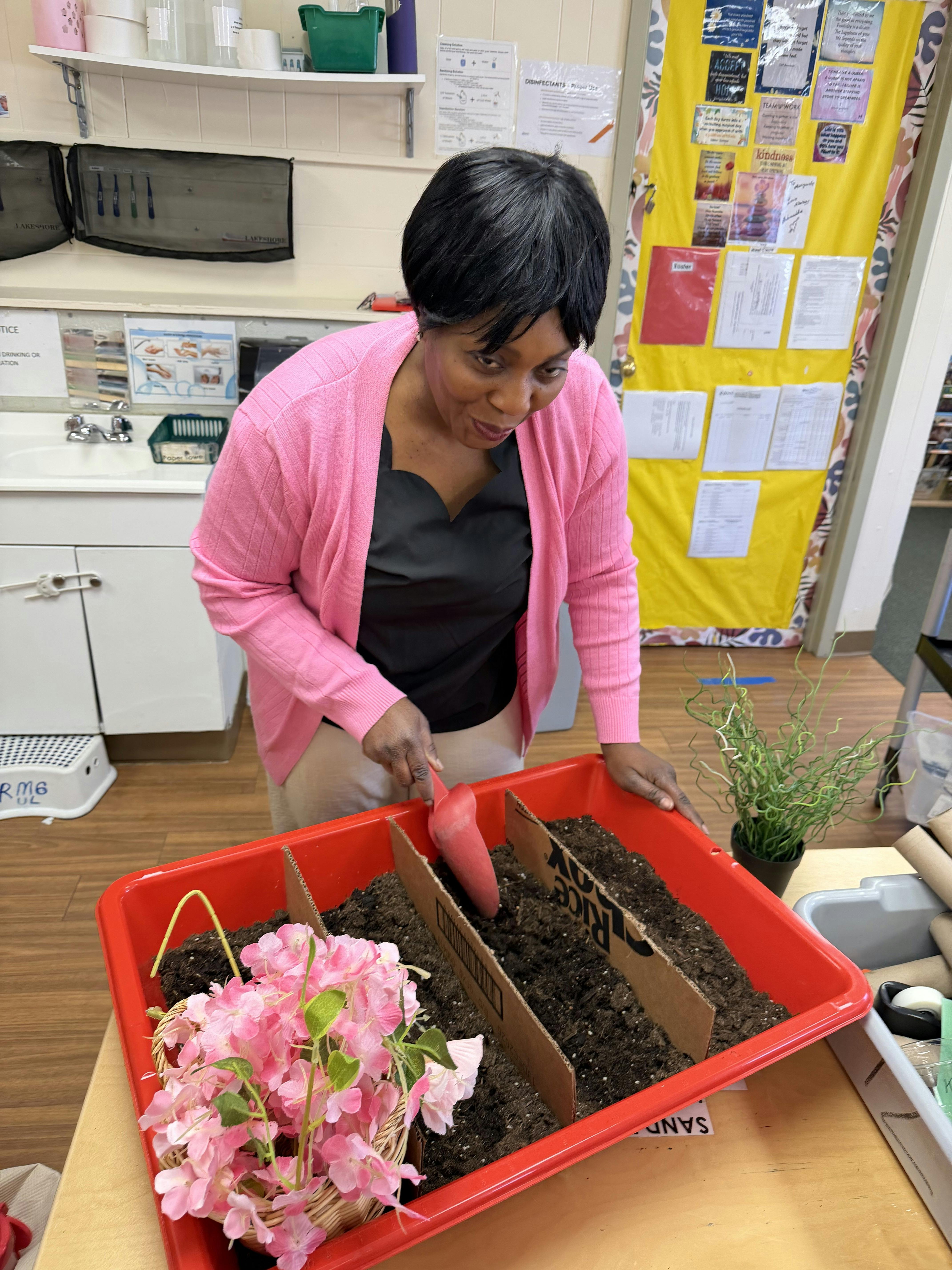 Person using a red trowel to scoop soil in a rectangular red tray