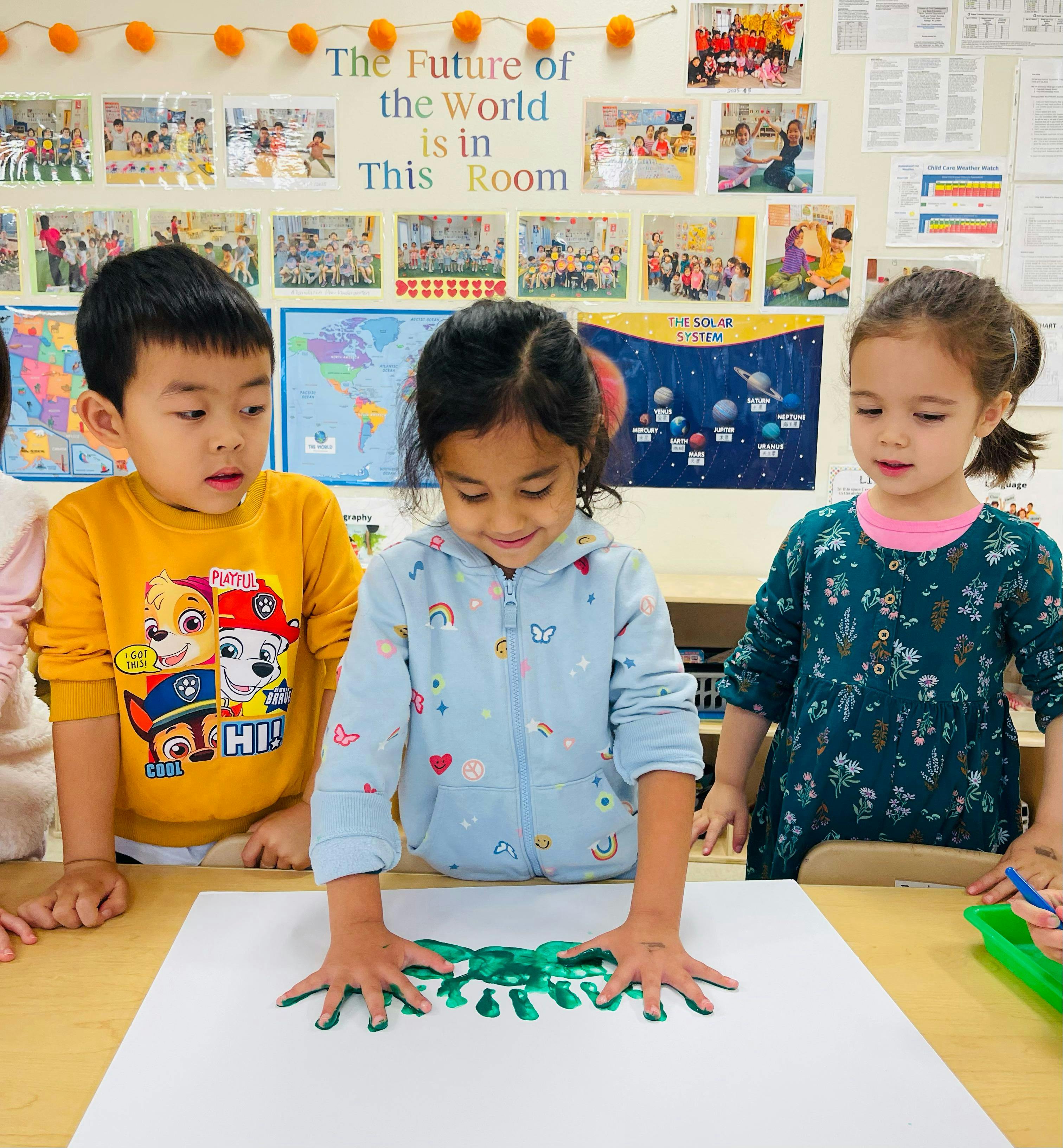 Three children finger painting at a table in a classroom