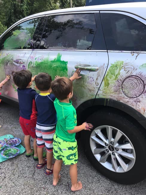 Three children finger painting on the side of a car