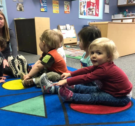 Adult and children sitting on a rug with shapes