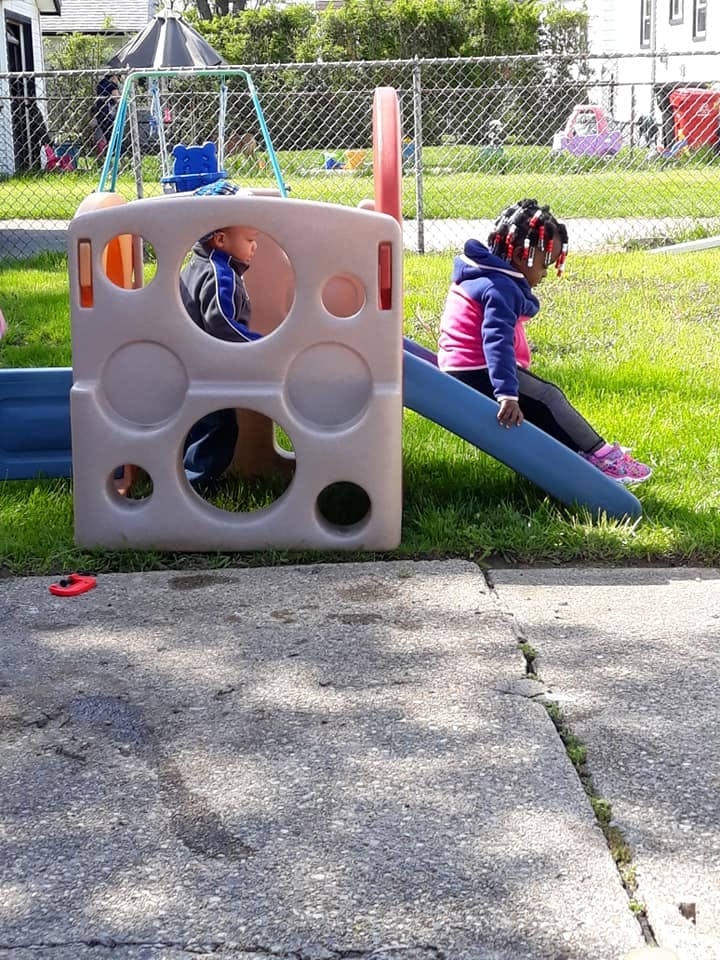 Two children playing on a small plastic playground slide and structure