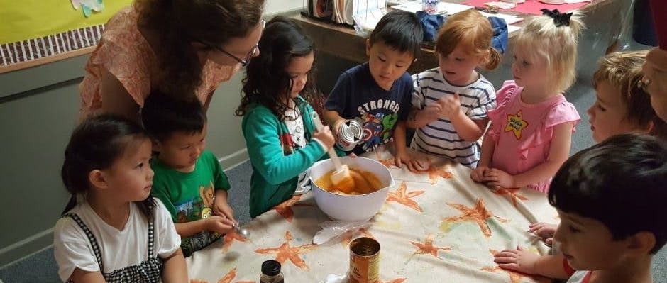 Adult and children gathered around a table mixing ingredients in a bowl