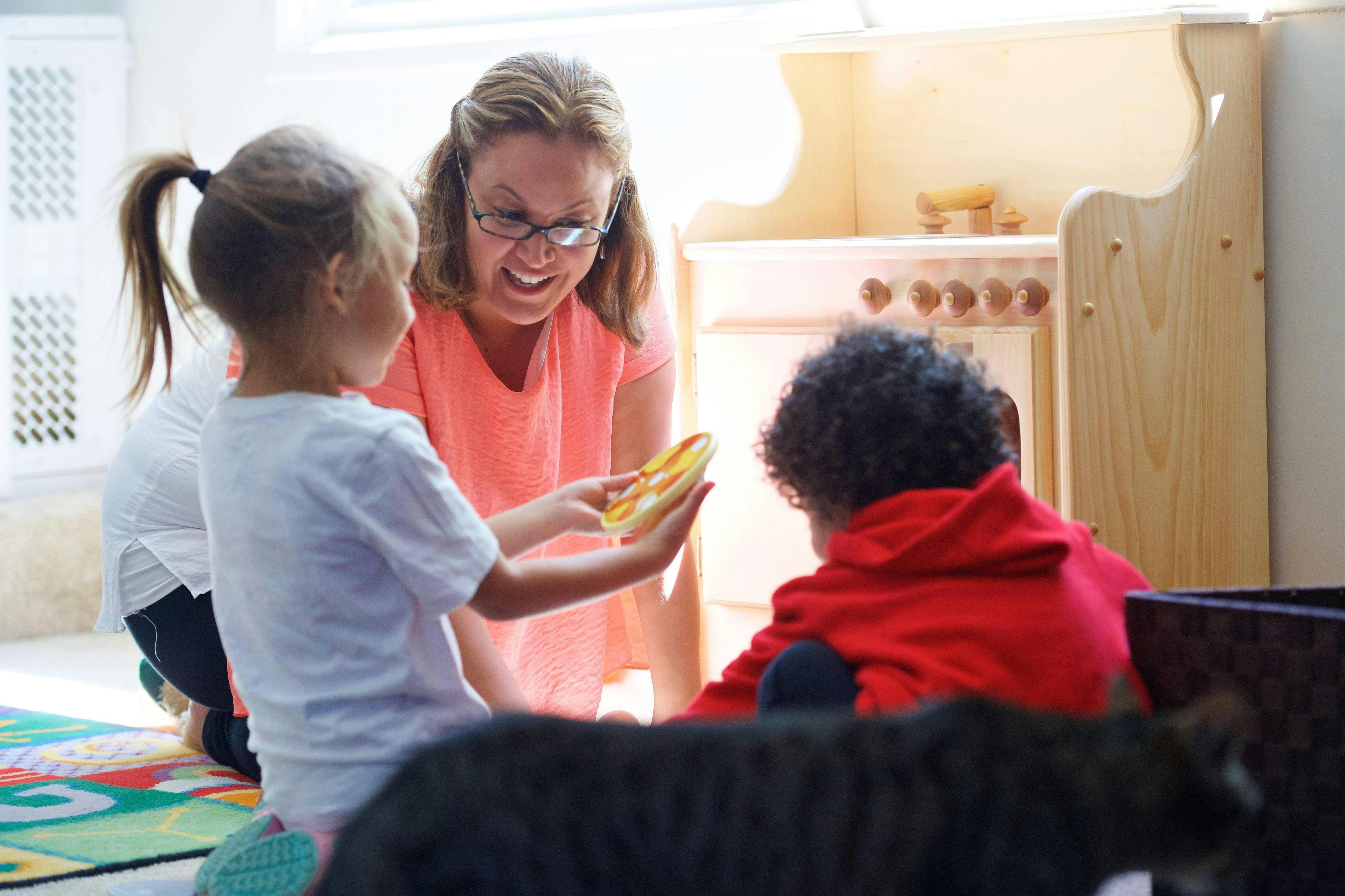 Adult and two children playing with a toy in a classroom