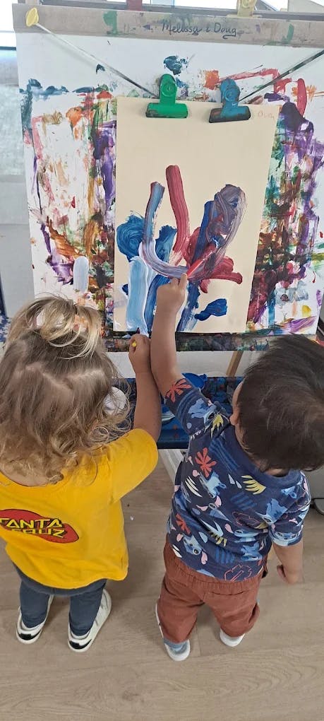 Two children painting together on an easel