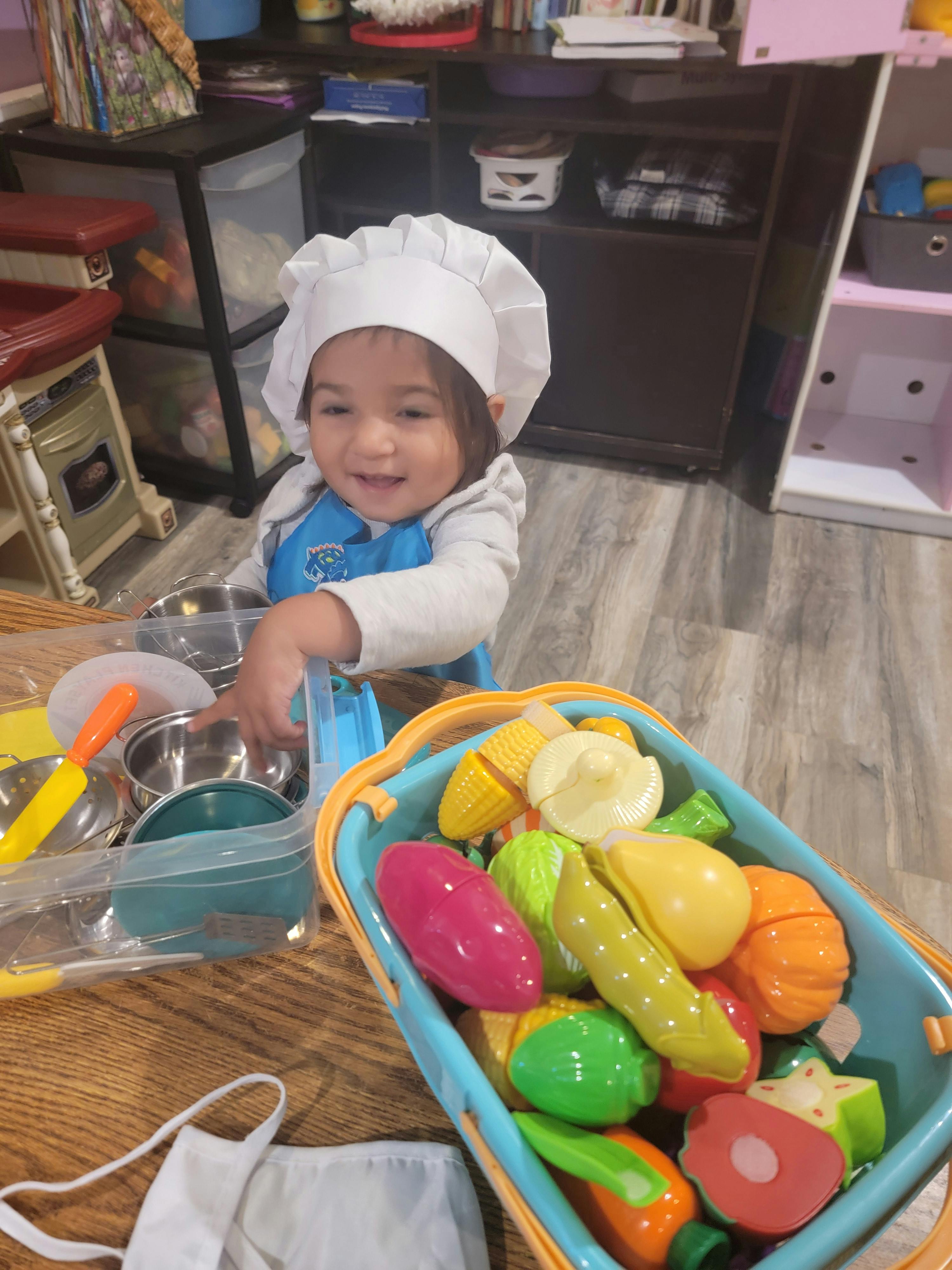 Child wearing a chef's hat playing with toy food and kitchenware