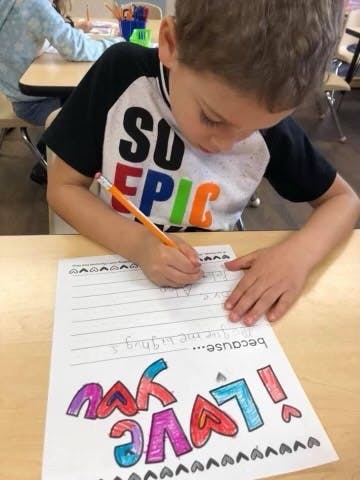 Child writing on a paper with "I LOVE YOU" text