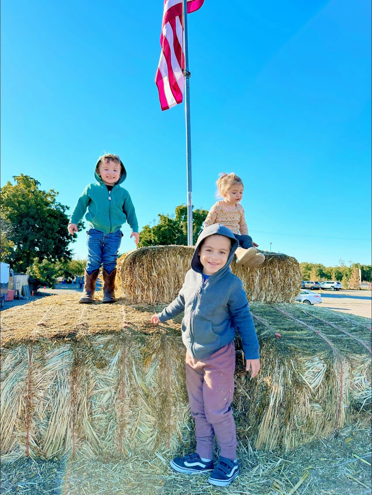 Three children on hay bales under an American flag