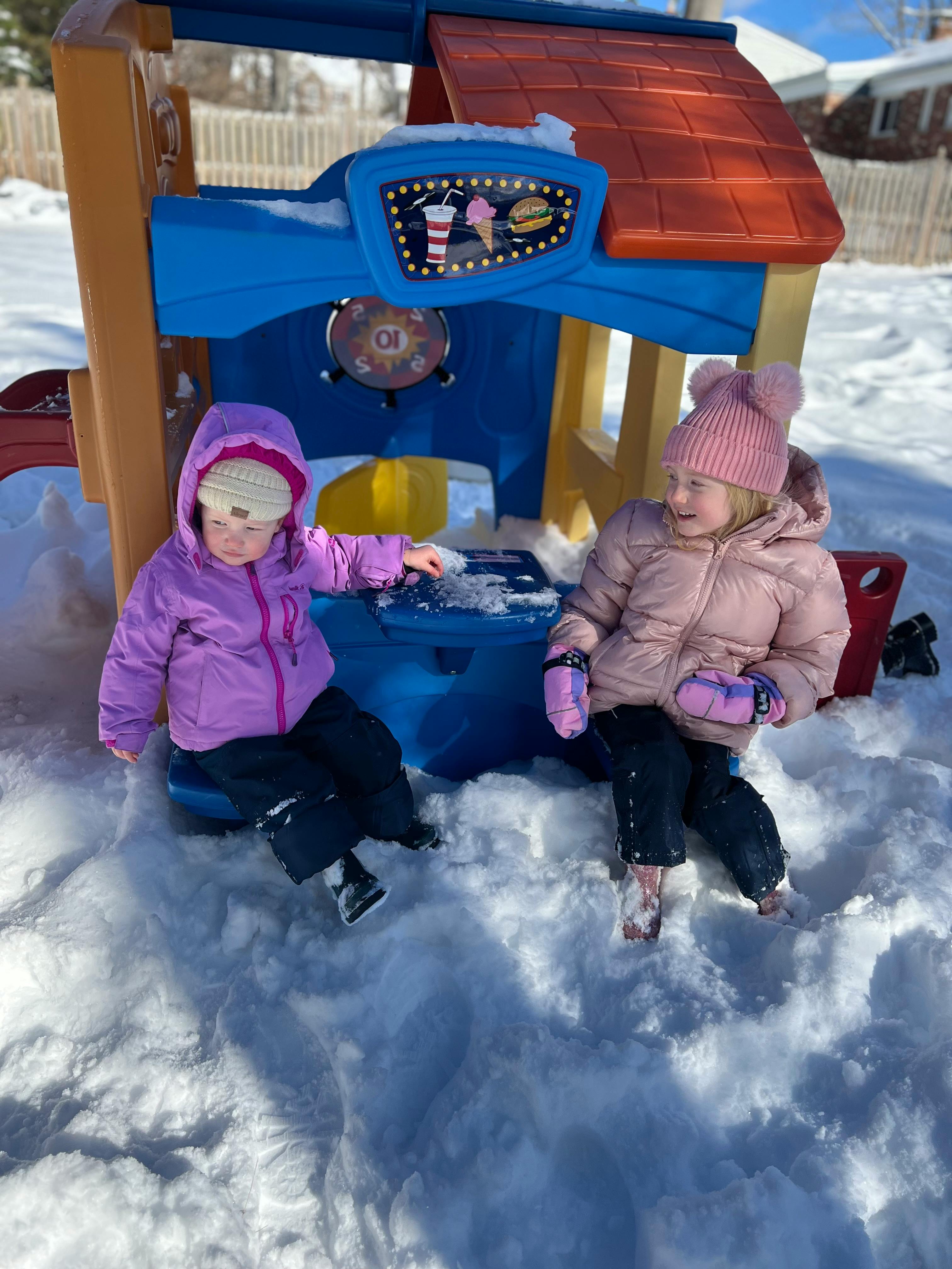 Two children playing in snow next to a playhouse