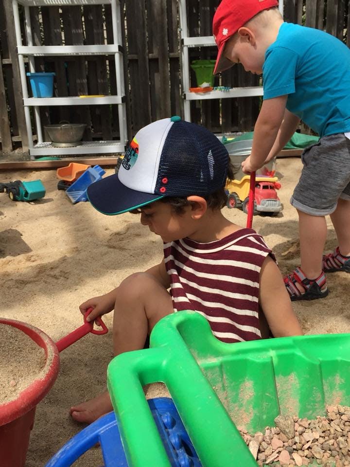 Two children playing in a sandbox with toys