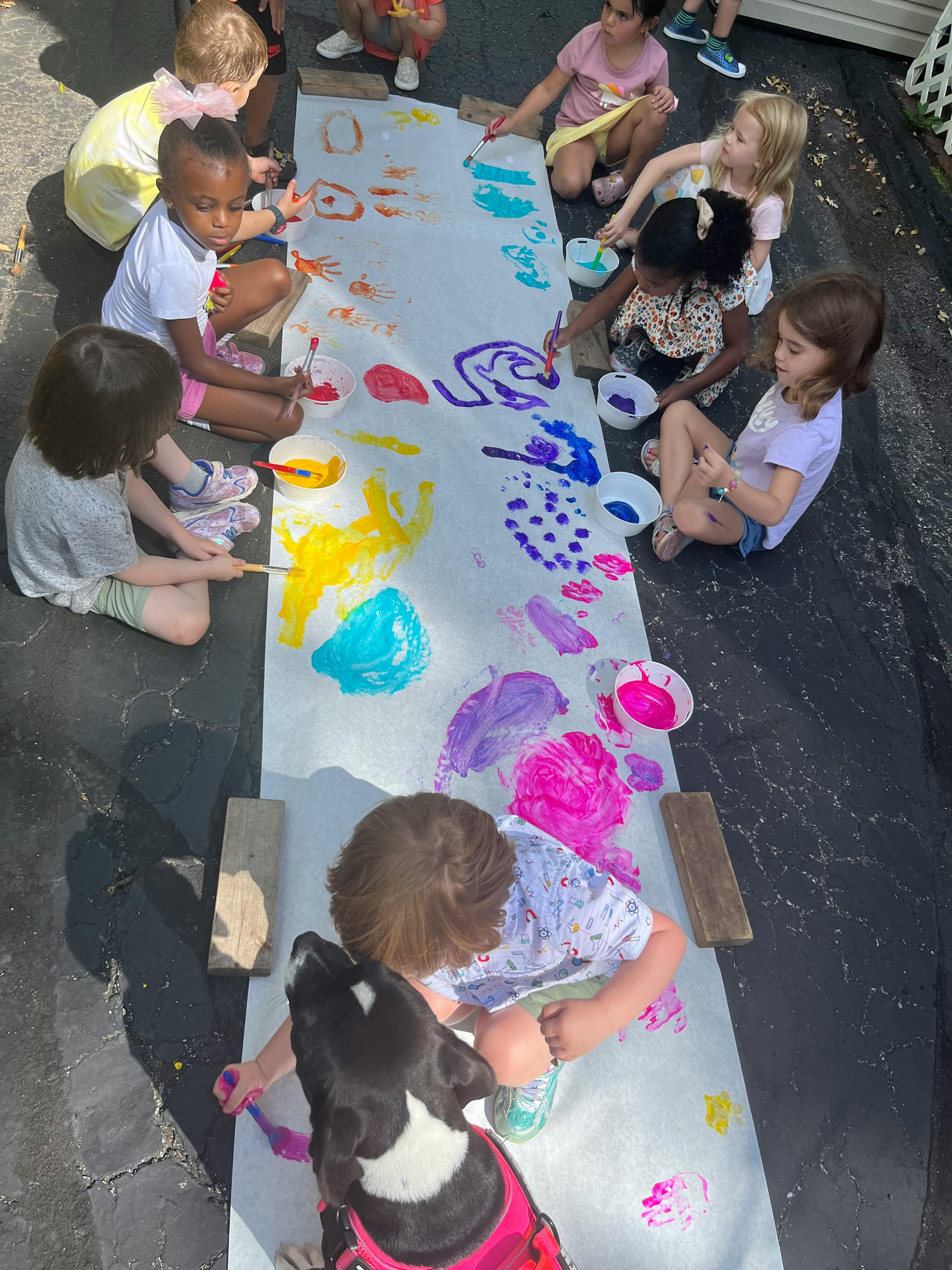 Children and a dog painting on a long sheet of paper outdoors