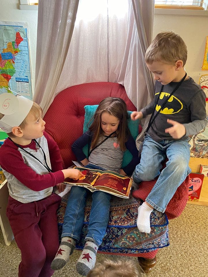 Three children reading a book together in a classroom