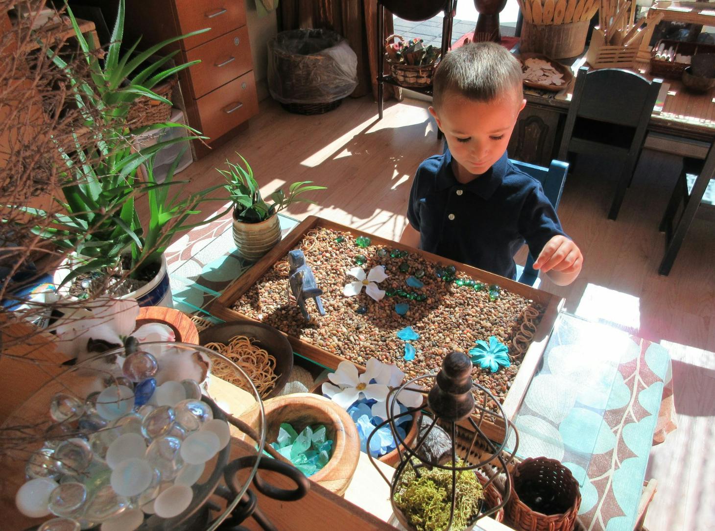 Child playing with a sensory bin filled with small pebbles and decorative items
