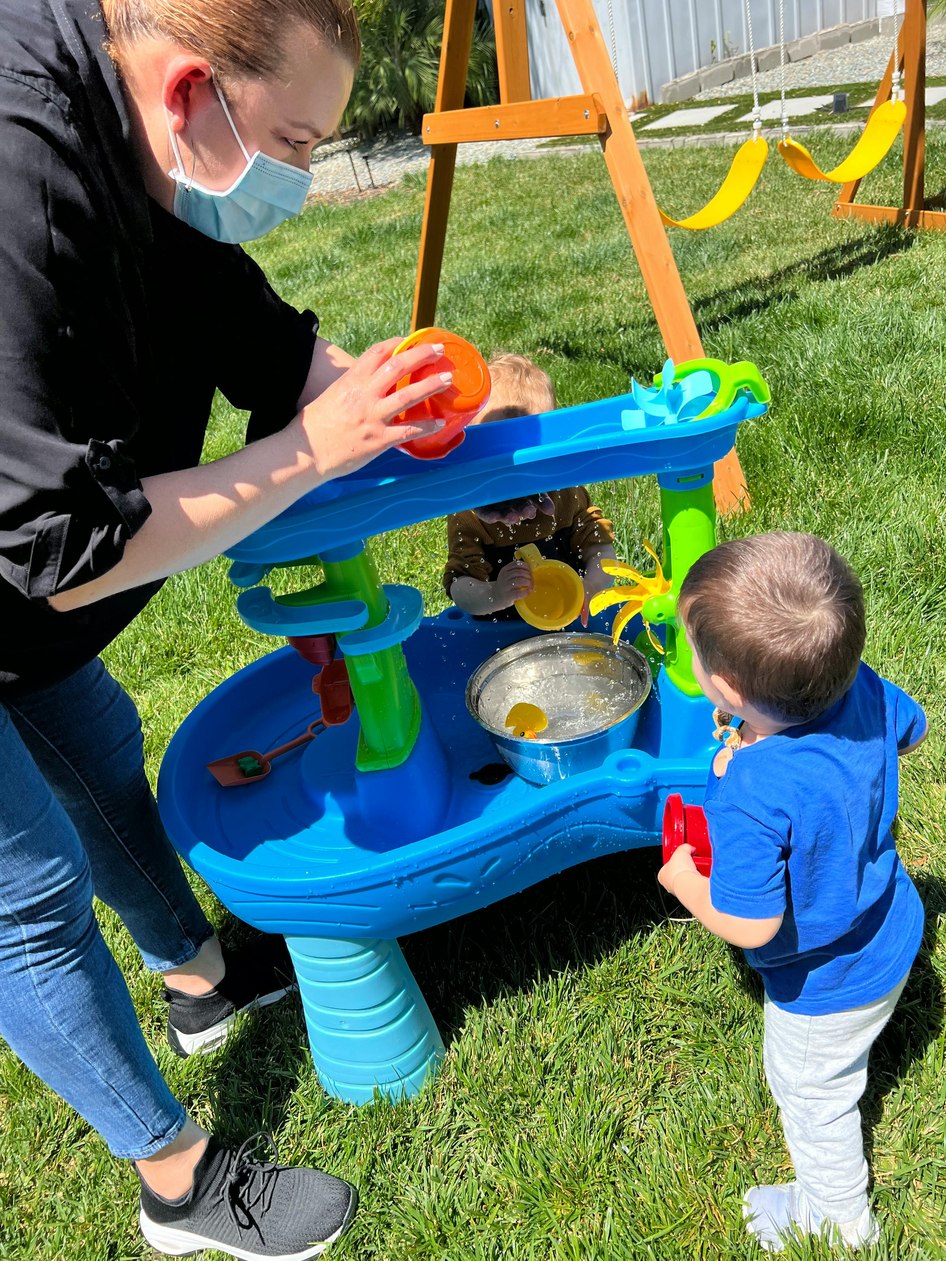 Person in mask and child playing with a water table outdoors