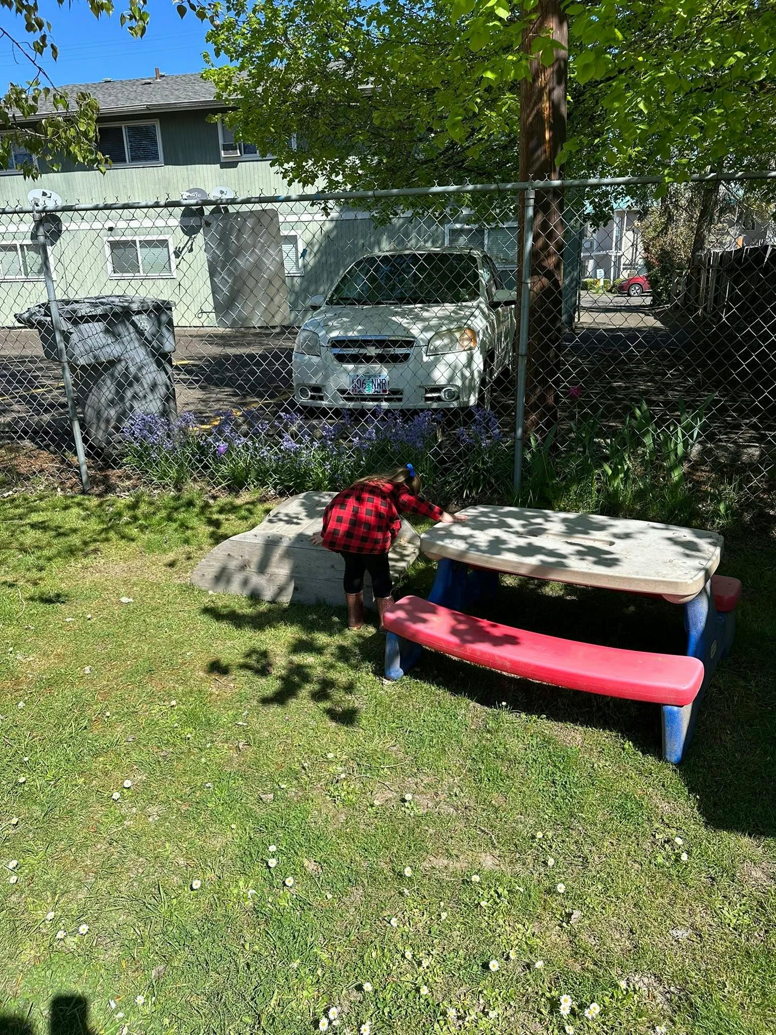 Child in plaid shirt standing by a small picnic table