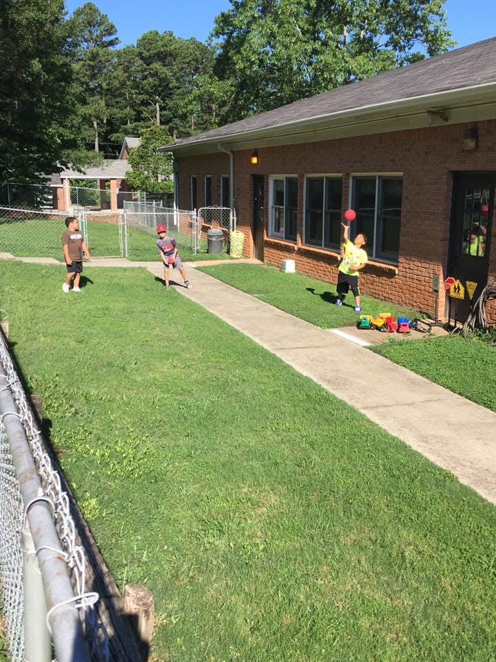 Three children playing with a ball on a grassy area next to a building