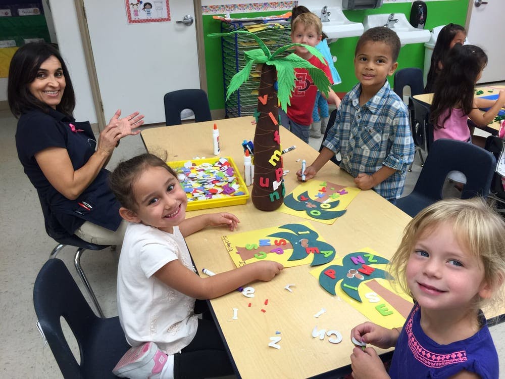 Adult and children doing crafts at a table in a classroom