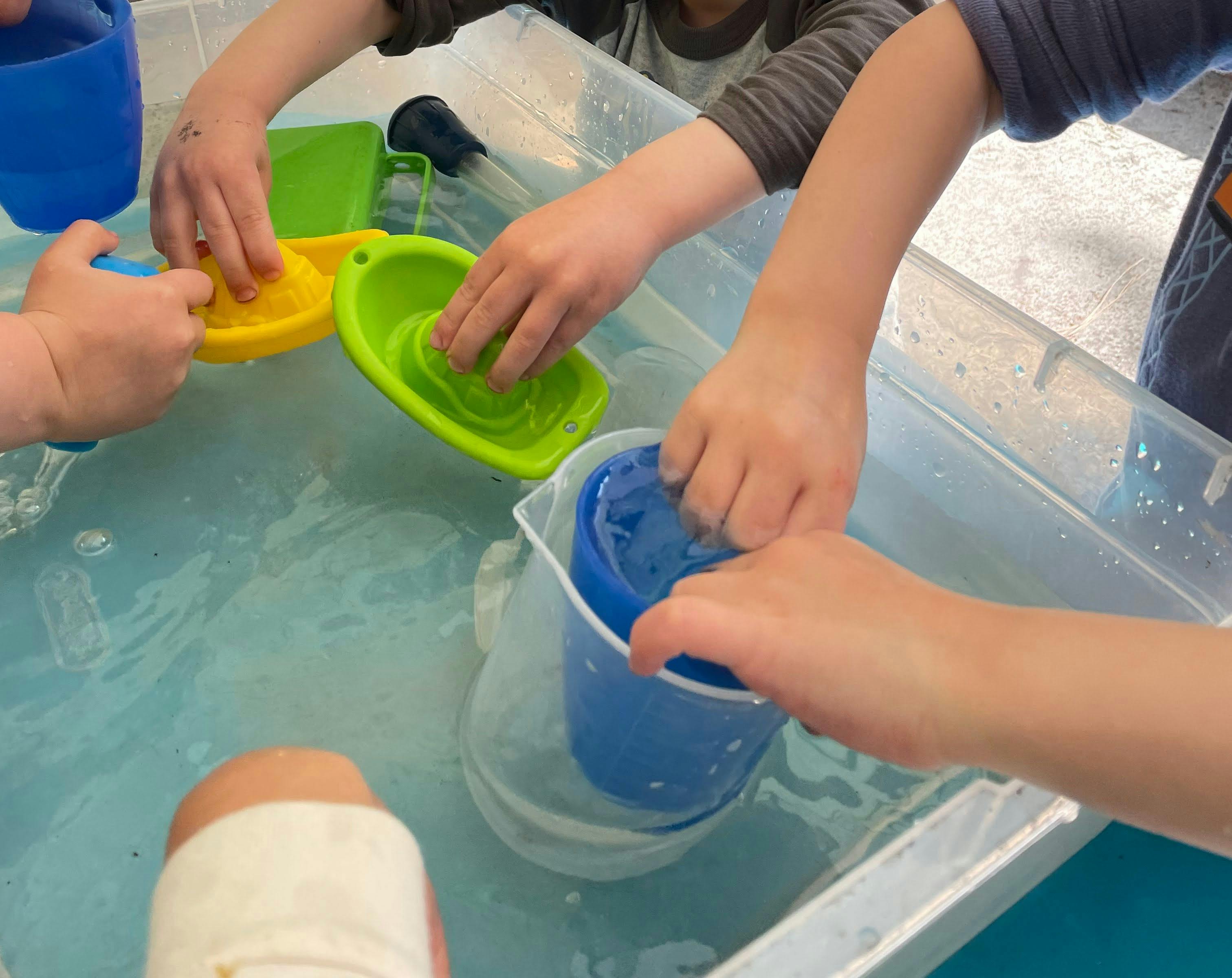 Children playing with water and plastic toys in a clear bin