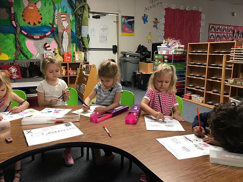 Children drawing and writing at a table in a classroom