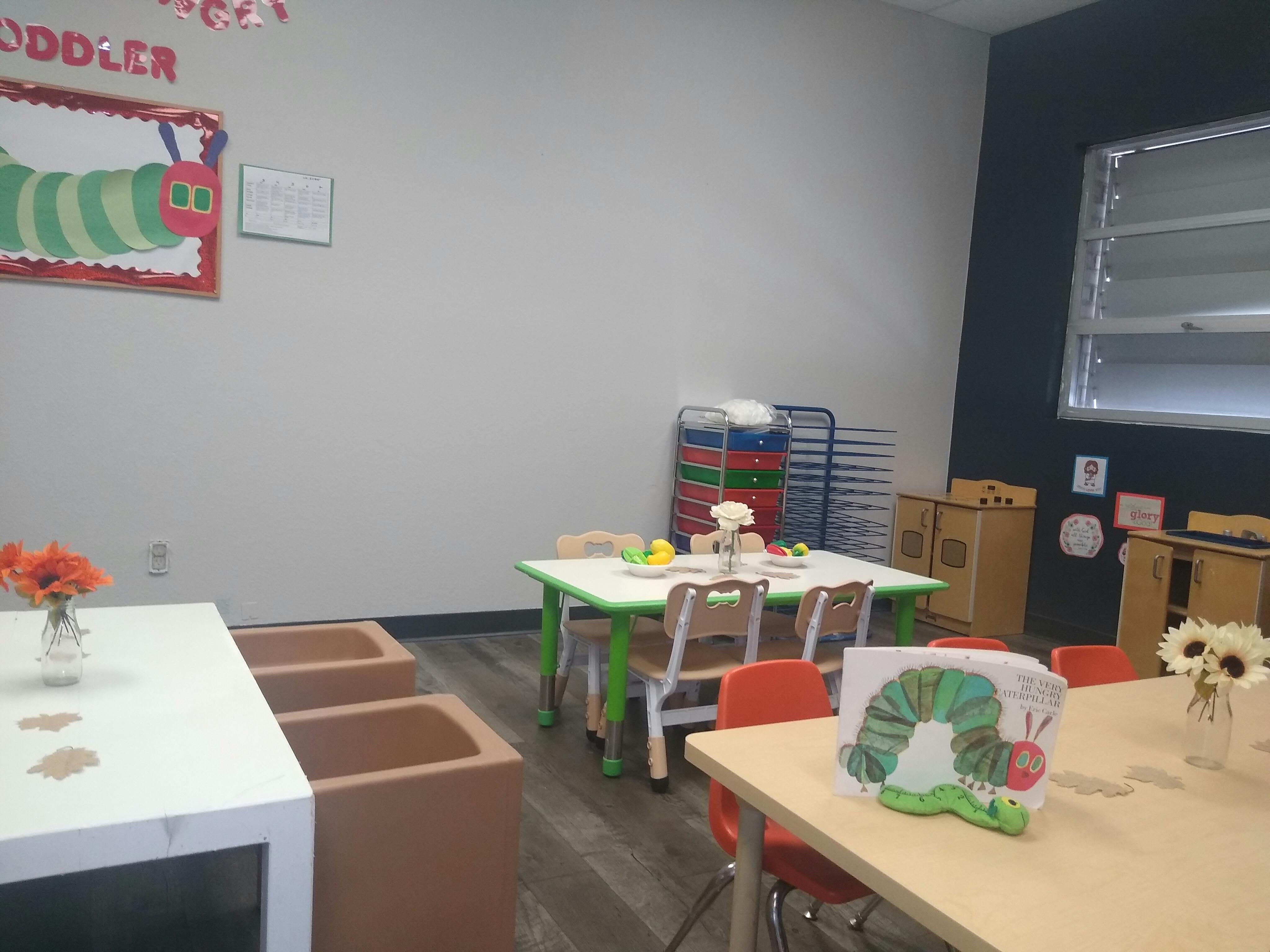 Classroom with small tables and chairs, and a caterpillar decoration on the wall