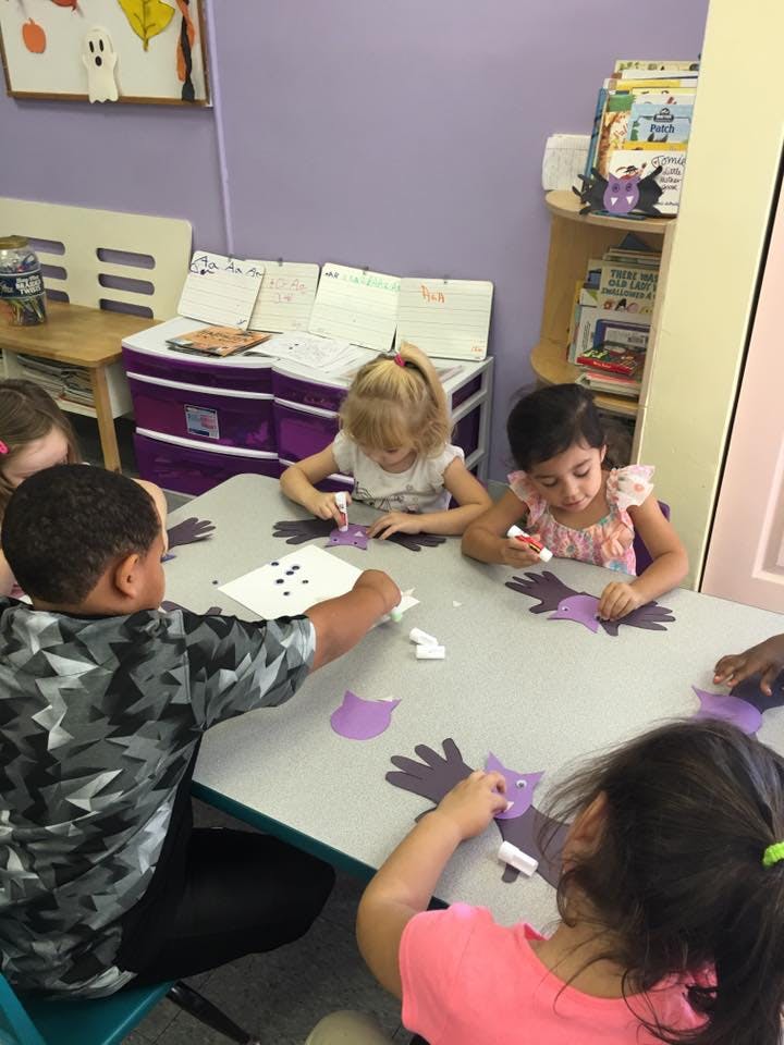 Children at a table doing crafts with paper cutouts and glue sticks
