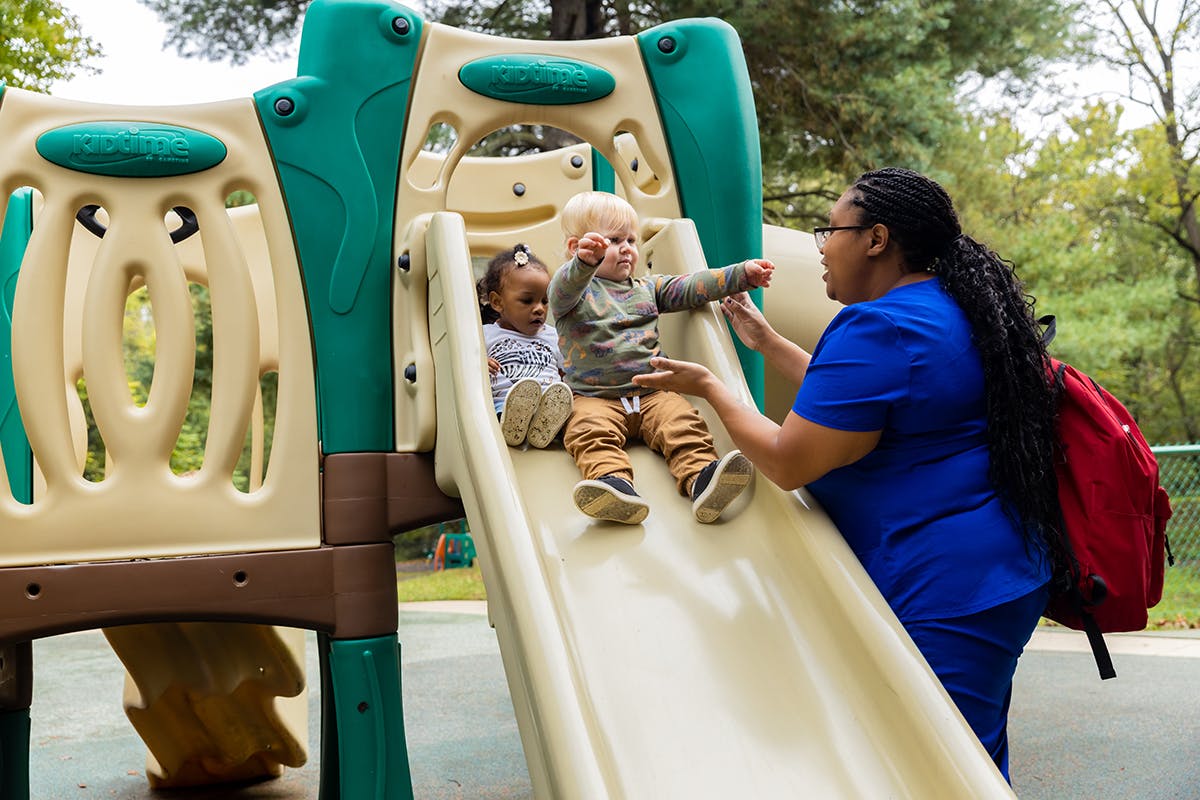 Adult helping two children on a playground slide