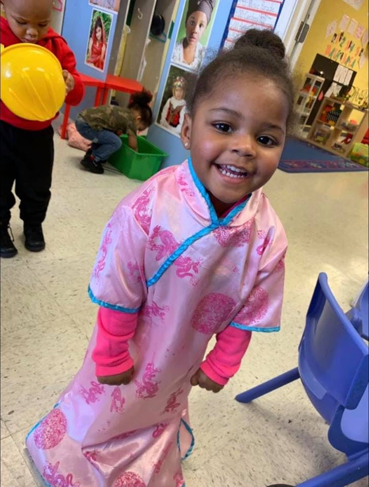 Child in pink dress smiling at camera in a classroom