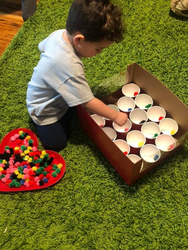 Child on green rug placing pom-poms into cups