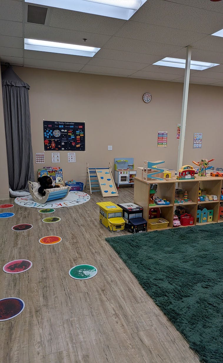 Children's play area with toys, a daily calendar on the wall, and a green rug
