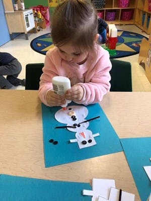 Child gluing pieces onto a paper snowman craft