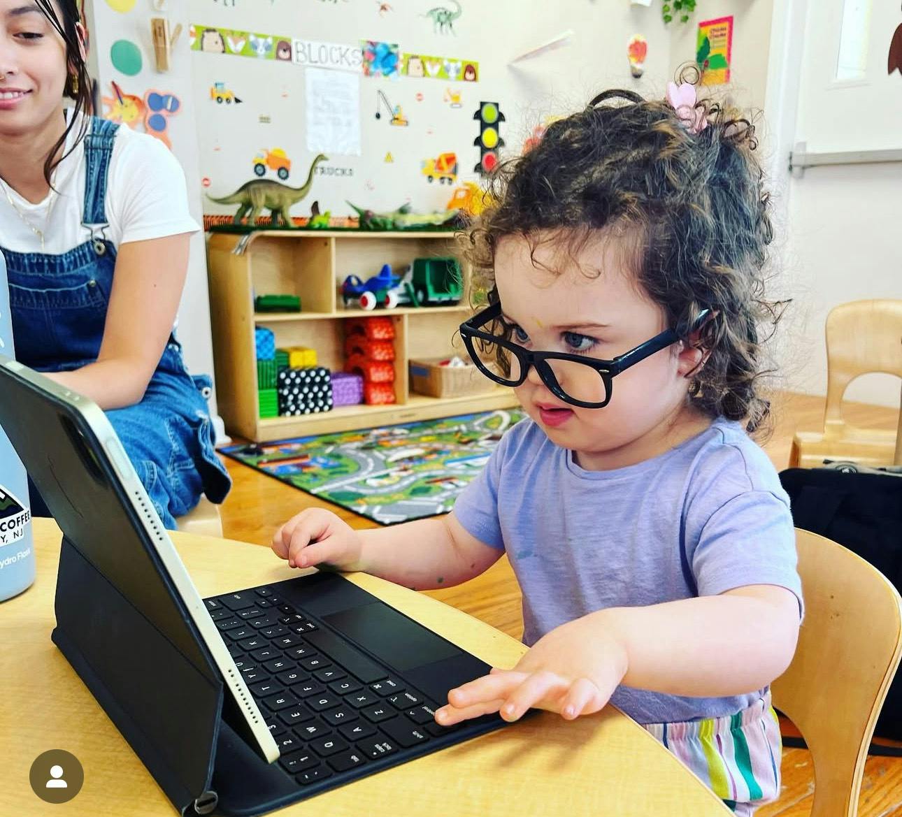 Child wearing glasses typing on a laptop in a classroom