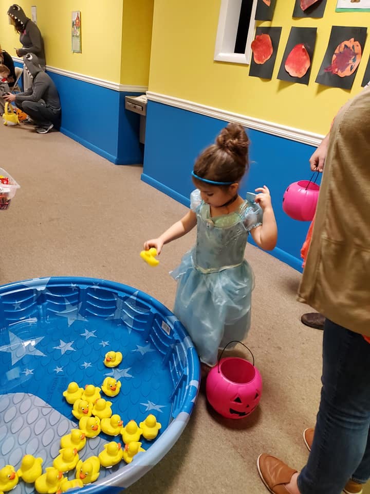 Child in a dress playing with rubber ducks in a blue pool