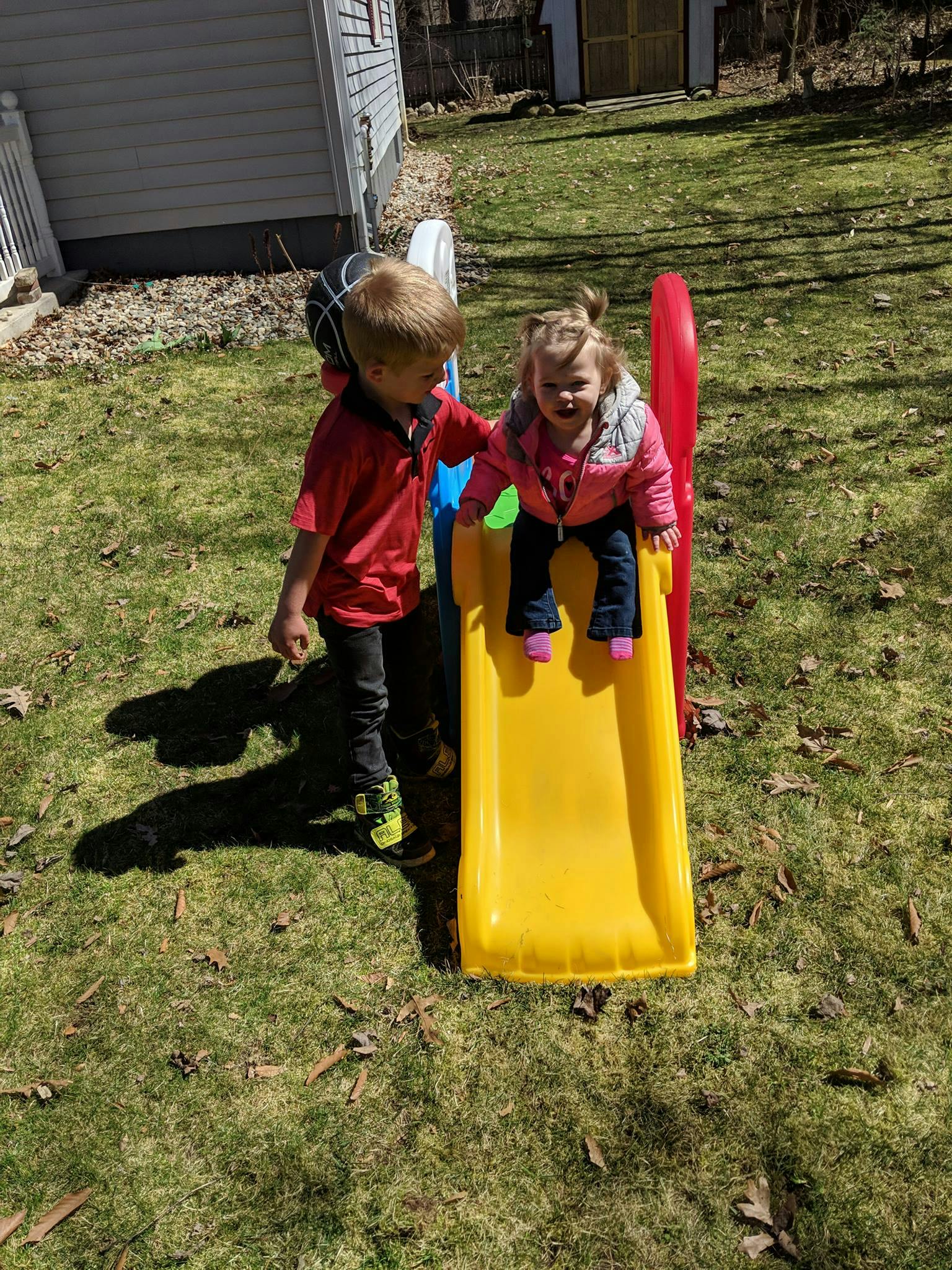 Child standing next to another child on a yellow slide