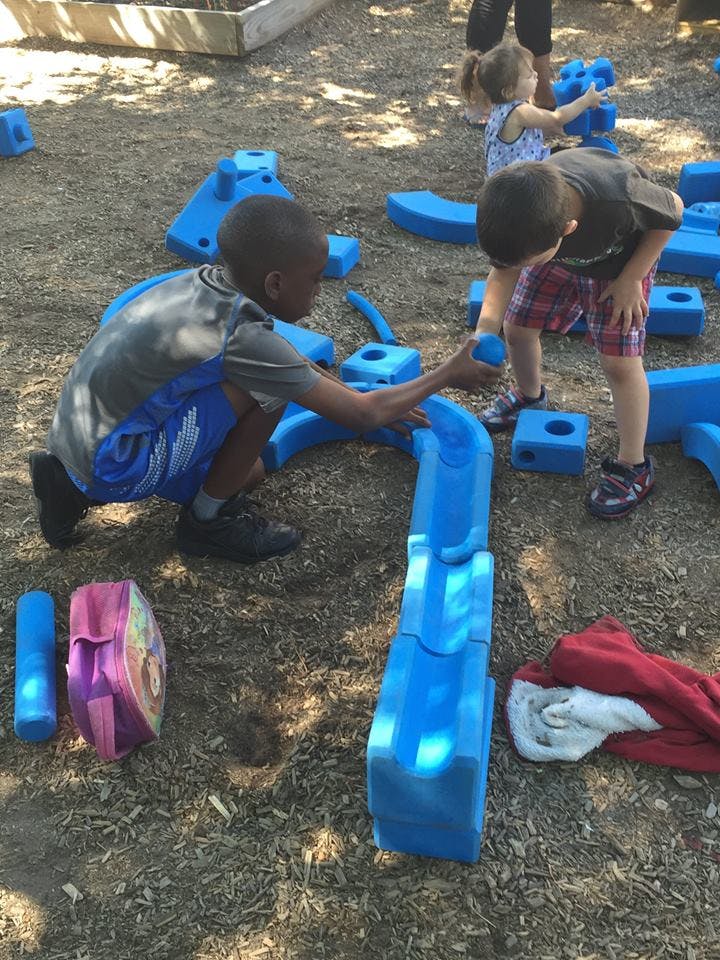 Two children playing with blue building blocks outdoors