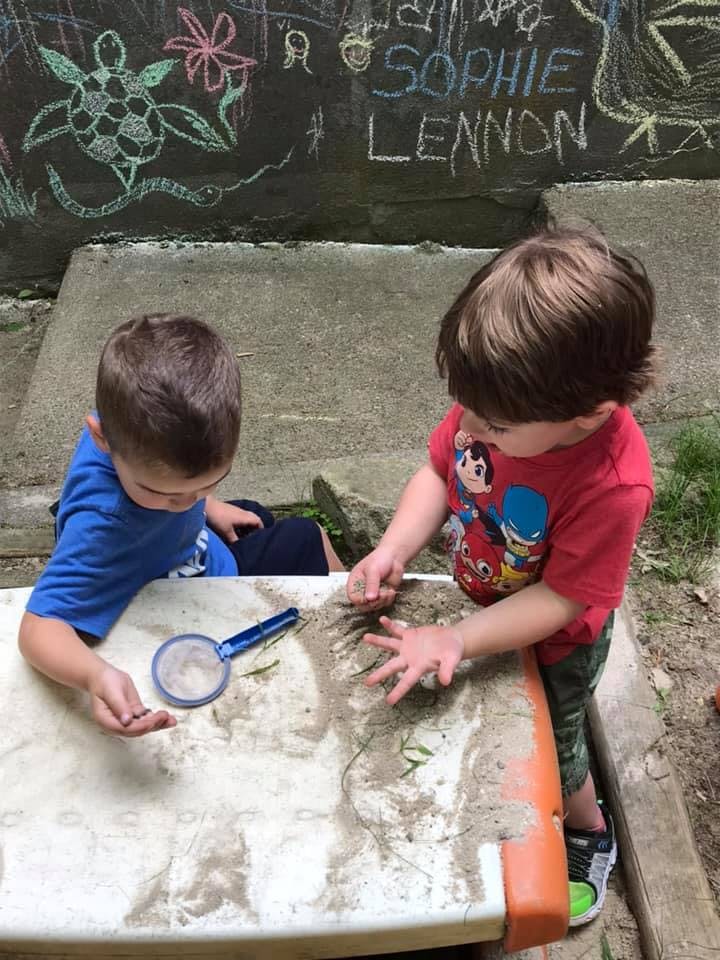 Two children playing with sand and a magnifying glass