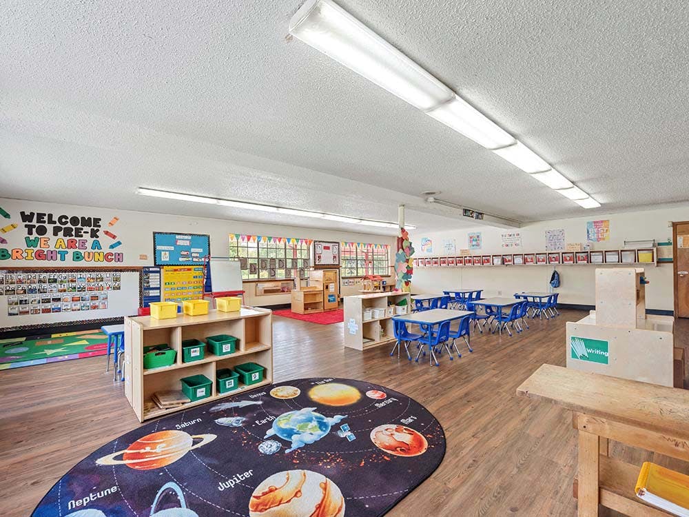 Empty preschool classroom with small tables and chairs, a solar system rug, and alphabet wall displays